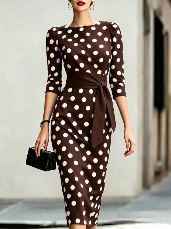 Woman wearing a brown dress with white polka dots, holding a black clutch.