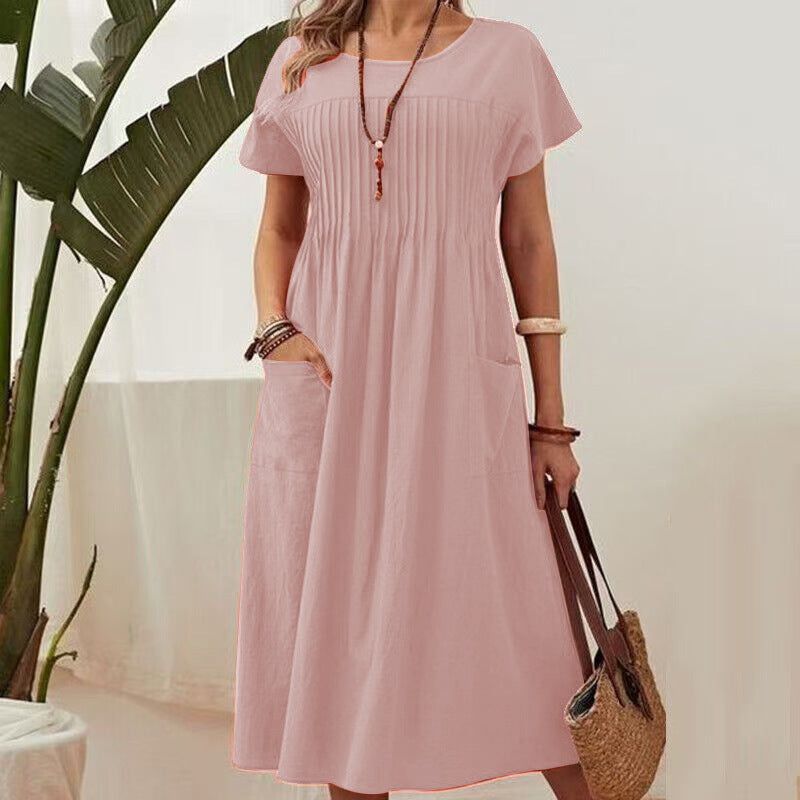 Woman wearing a pink dress holding a straw bag indoors with a plant in the background