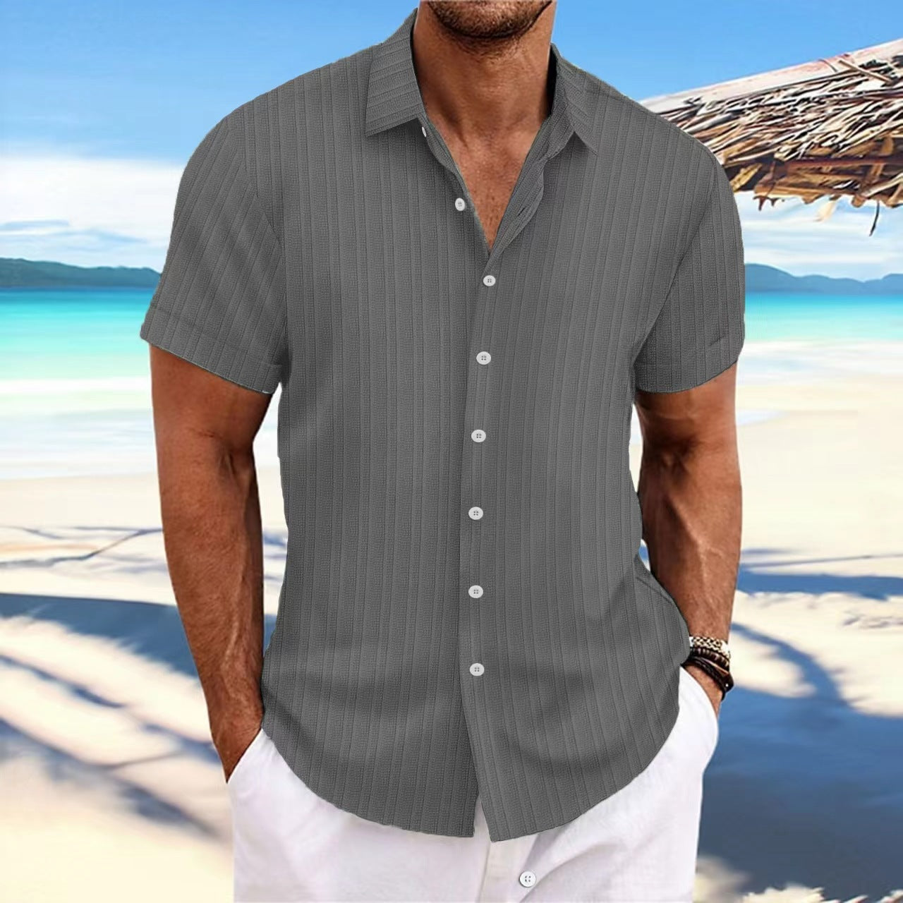 Man wearing a gray striped shirt on a beach with ocean and sky in the background