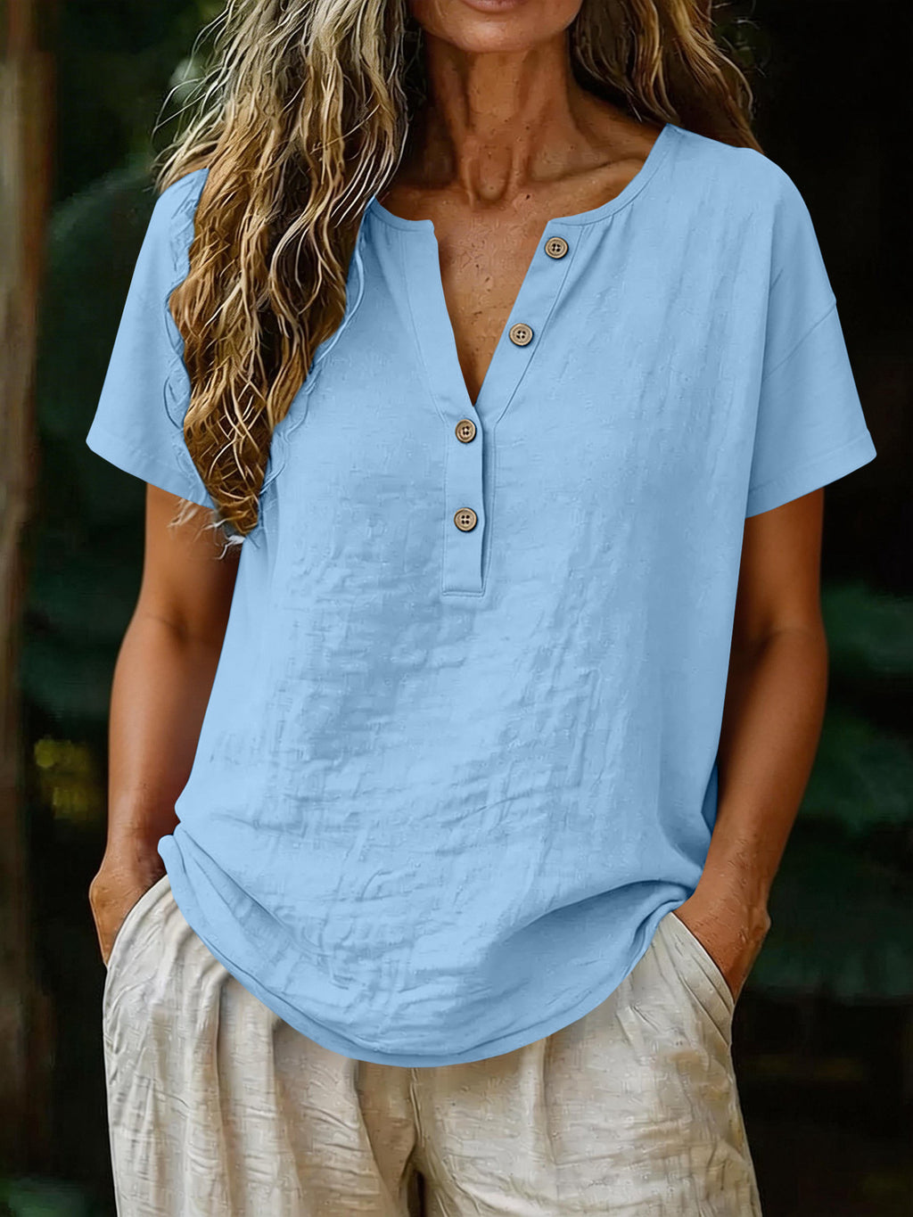 Person wearing a light blue shirt with button details and beige pants against a blurred natural background