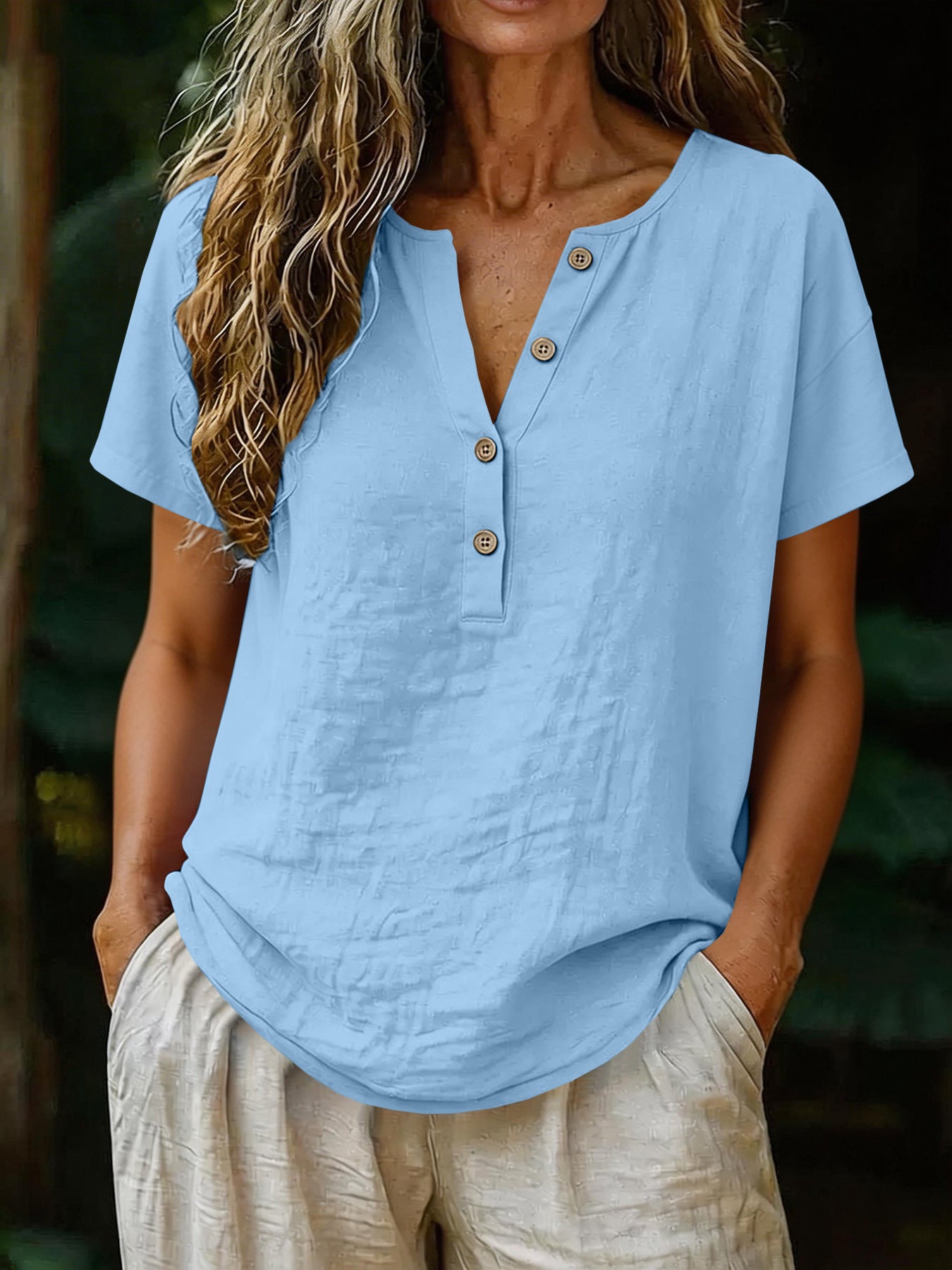 Person wearing a light blue shirt with button details and beige pants against a blurred natural background