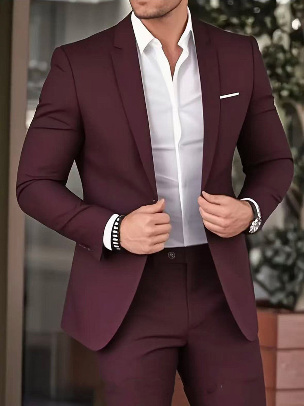 Man wearing a burgundy suit with a white shirt, standing against an outdoor background.