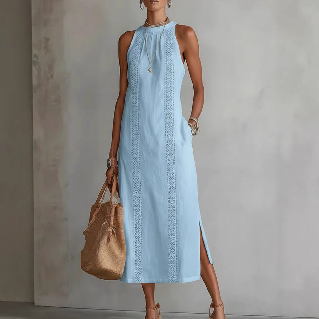 Woman wearing a light blue dress with intricate patterns, holding a beige handbag against a neutral background.