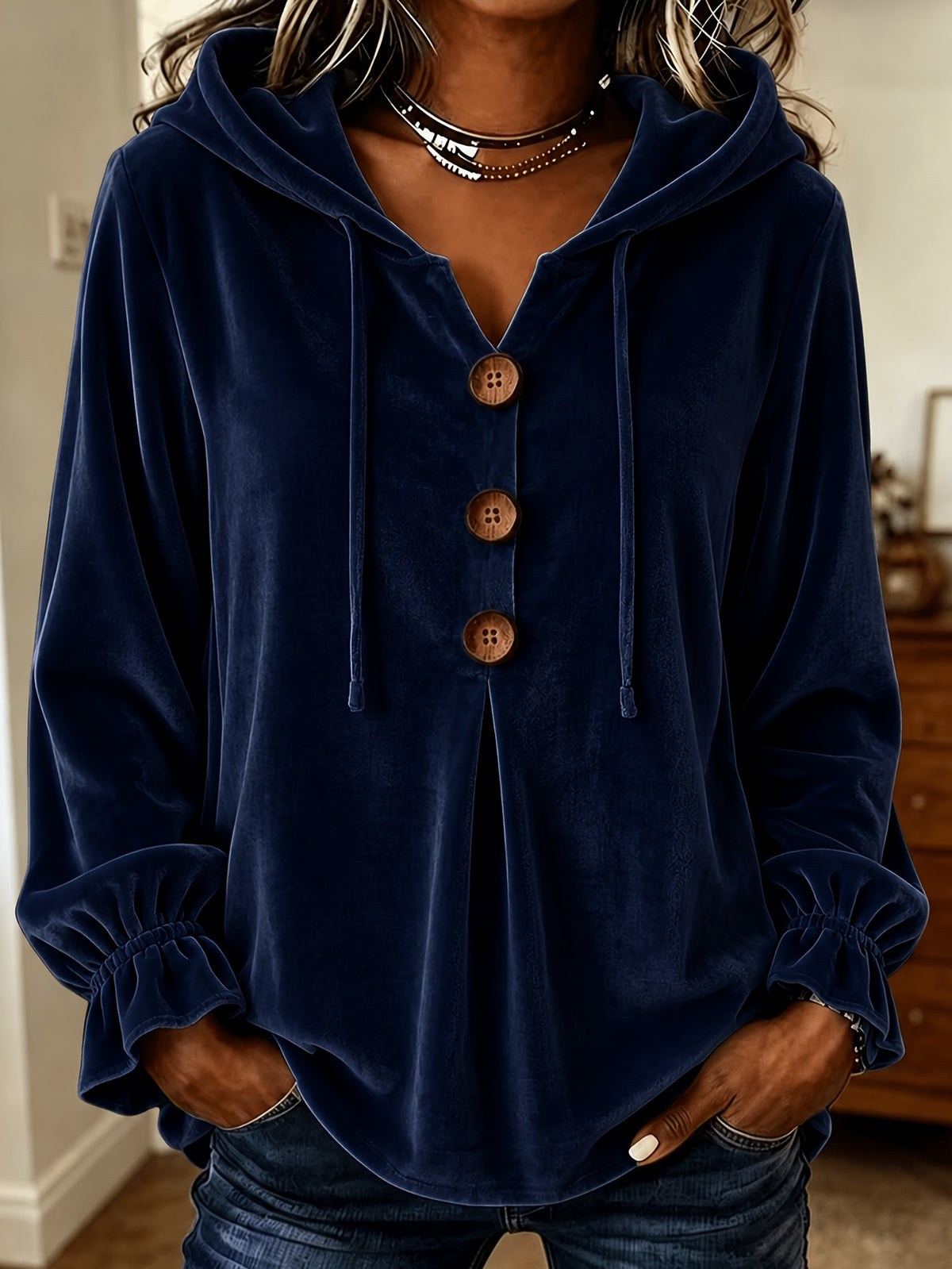 A woman wearing a navy blue velvet hooded sweatshirt with three brown buttons down the front, paired with dark blue jeans.