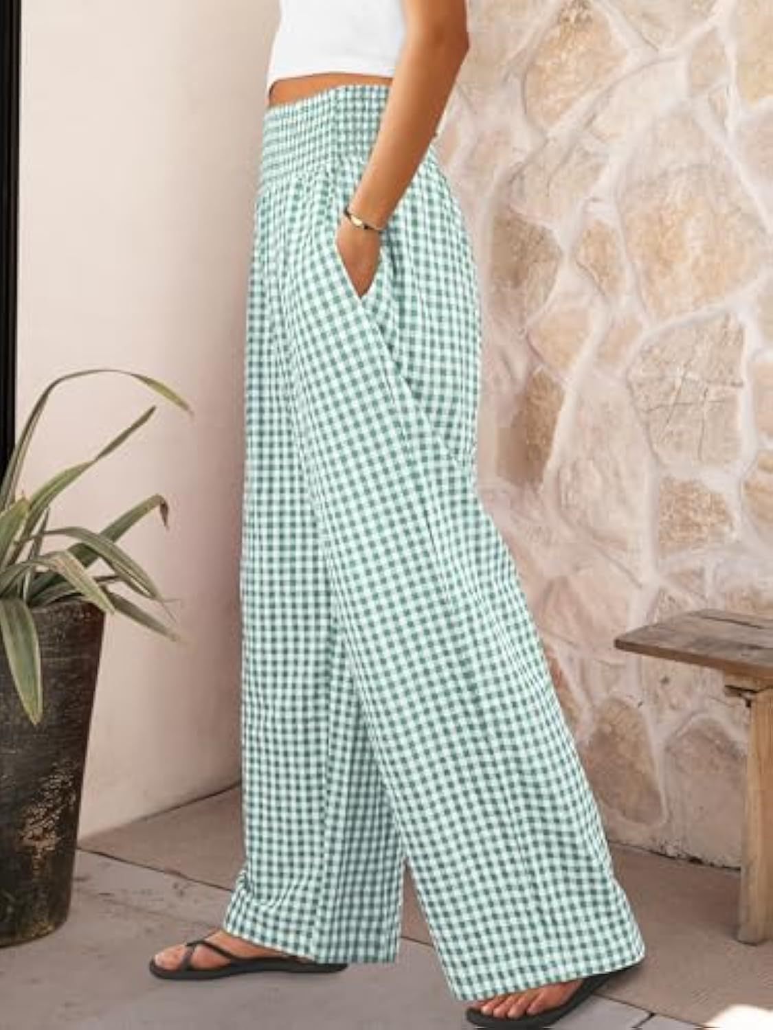 Person wearing green checkered pants standing against a stone wall.