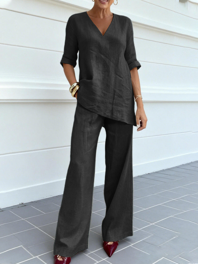 Person wearing a dark gray outfit with wide-leg pants against a white wall.