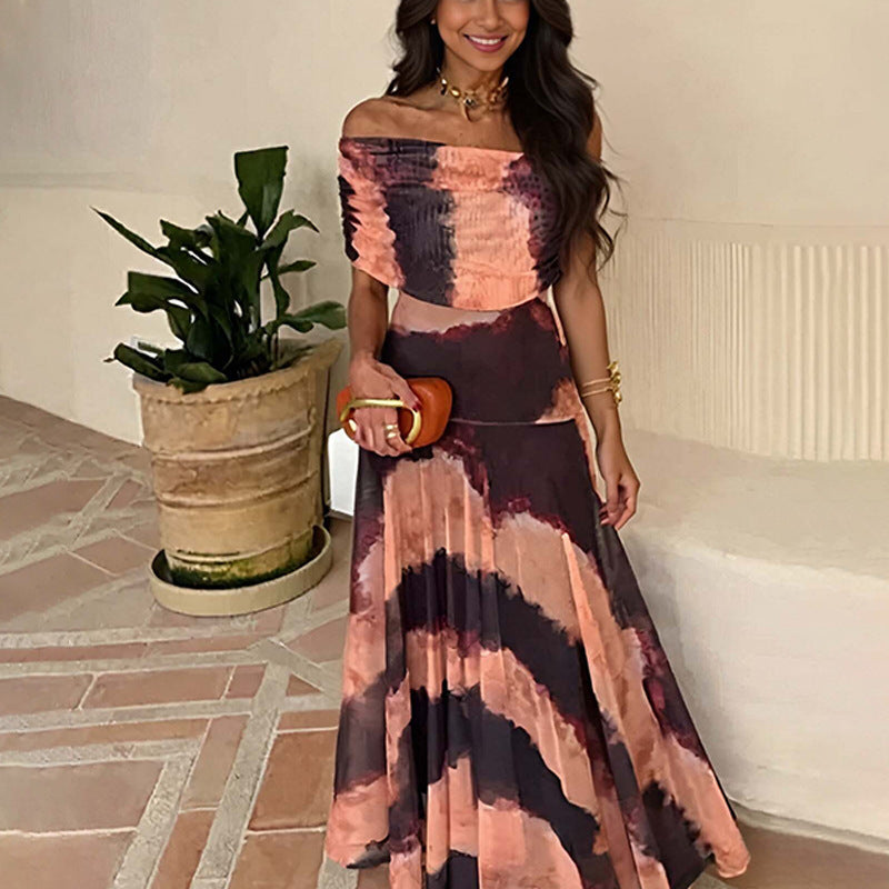Woman wearing a tie-dye dress holding a clutch, standing indoors with a plant in the background.