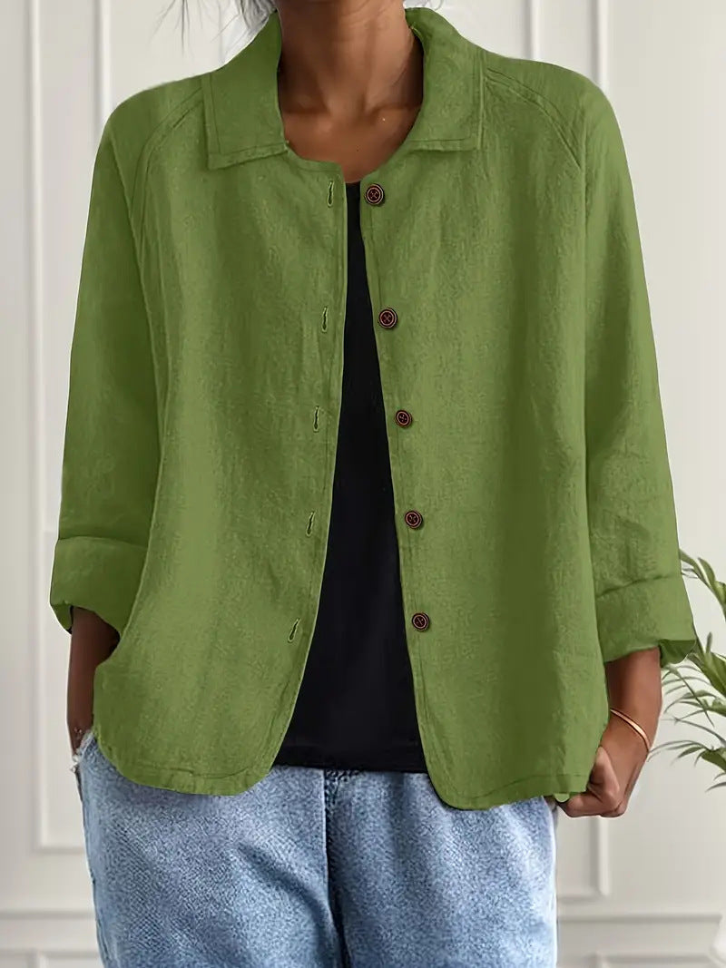 Person wearing a green jacket over a black top and blue jeans against a white wall.