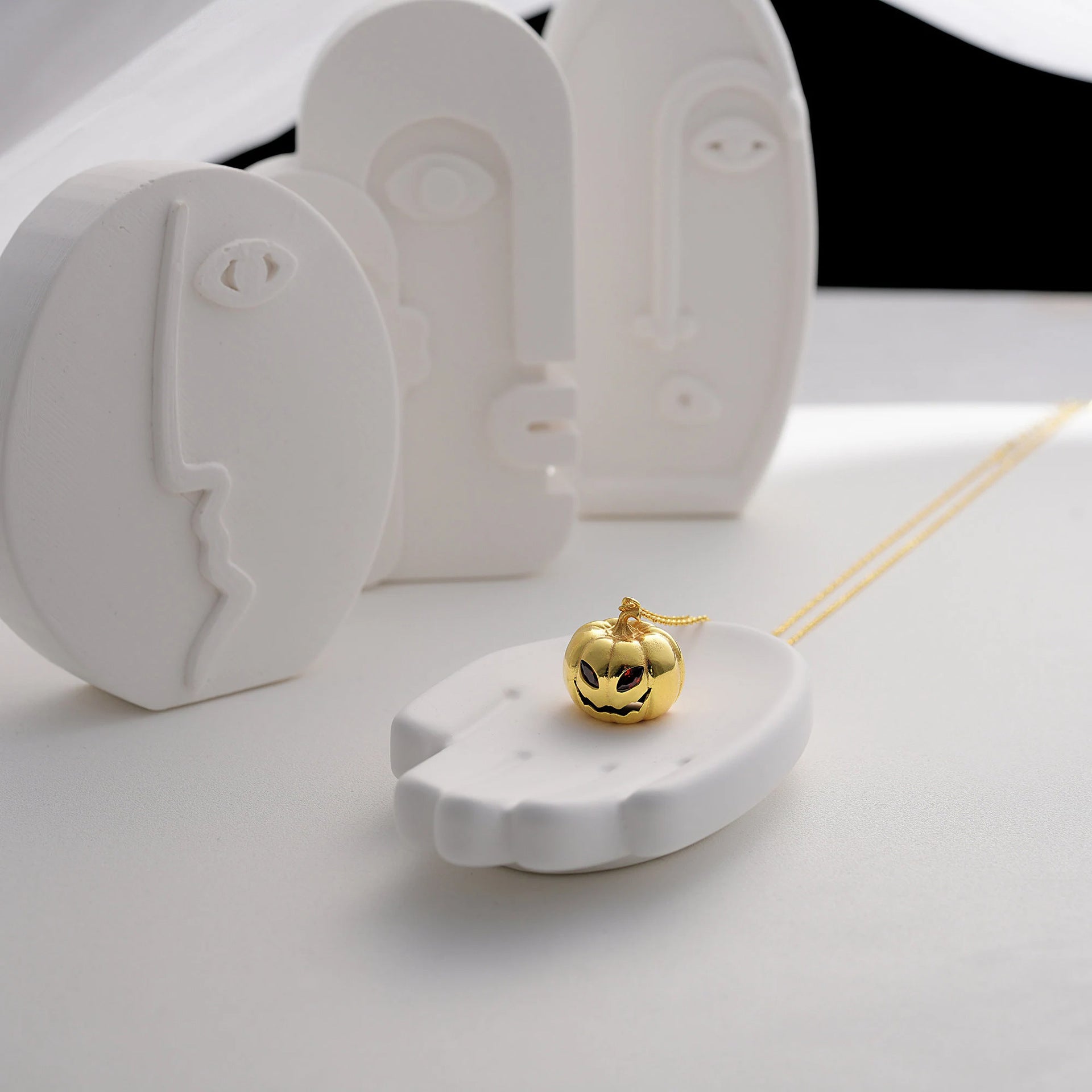Gold pumpkin-shaped pendant on a white stand with a white background