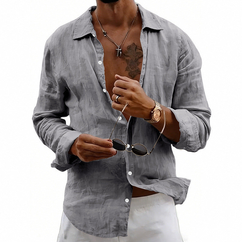 Man wearing a light gray button-up shirt with rolled-up sleeves, holding sunglasses.