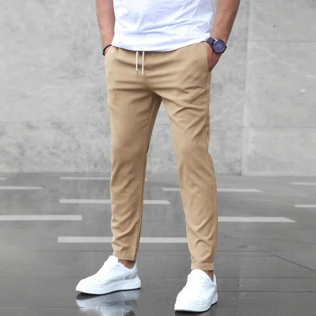 Person wearing beige pants and white sneakers against a gray background