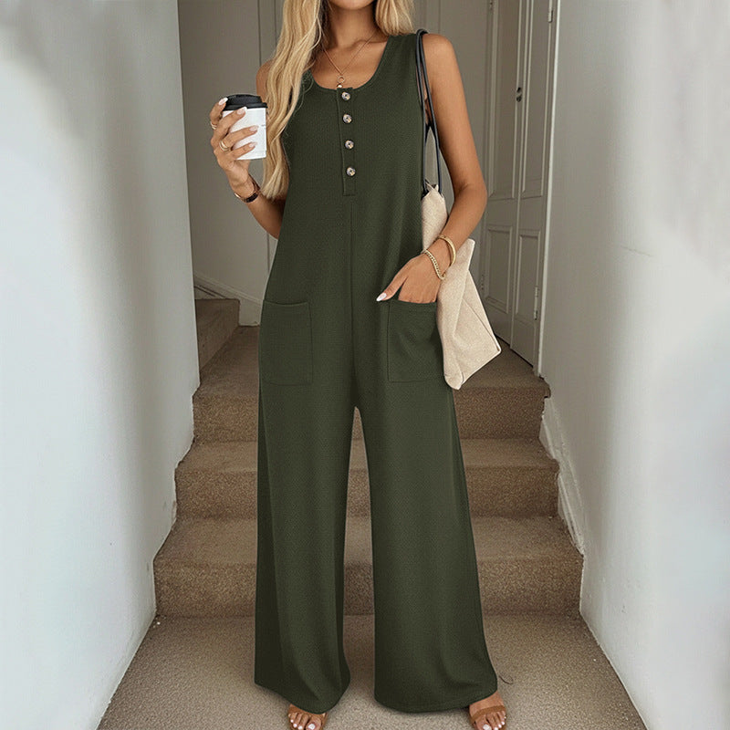 Woman in green jumpsuit holding a coffee cup and a beige bag on a staircase.