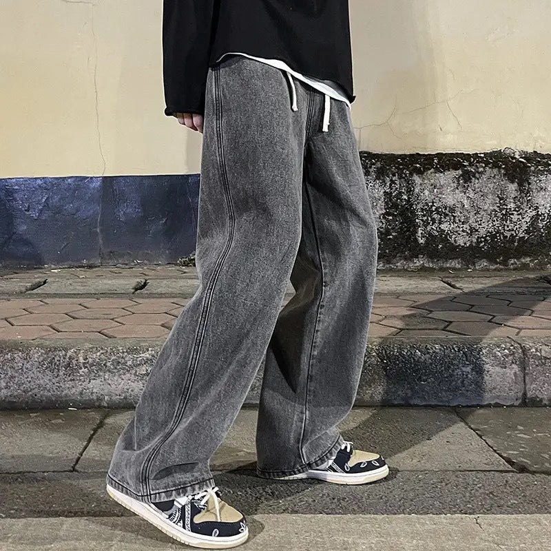 Person wearing gray wide-leg jeans and black sneakers on a sidewalk.