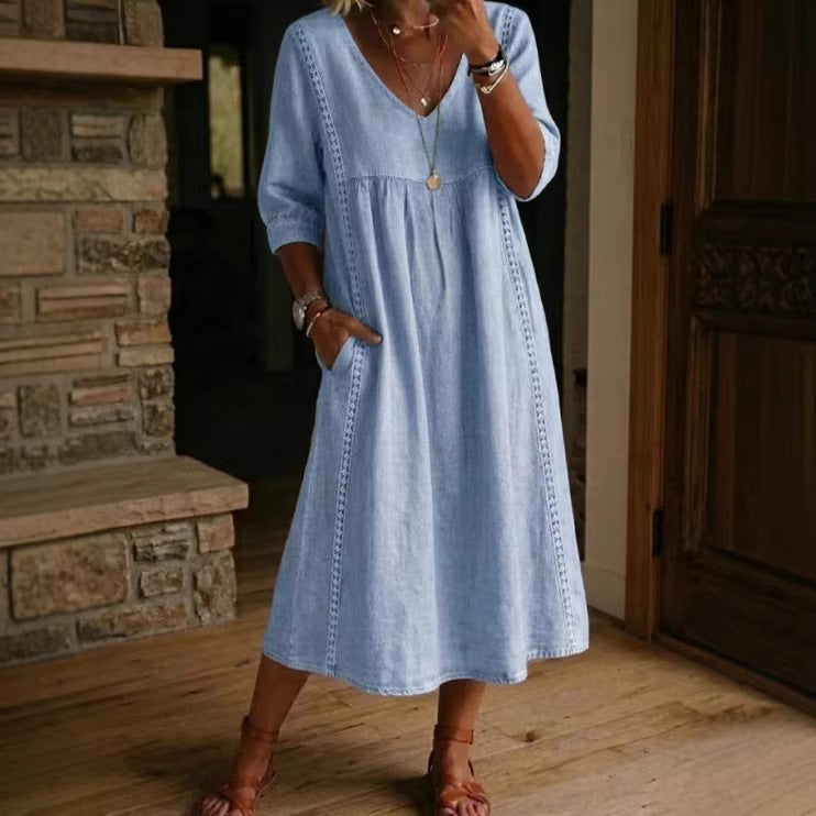 Woman wearing a light blue dress standing in a room with wooden flooring and a stone fireplace.
