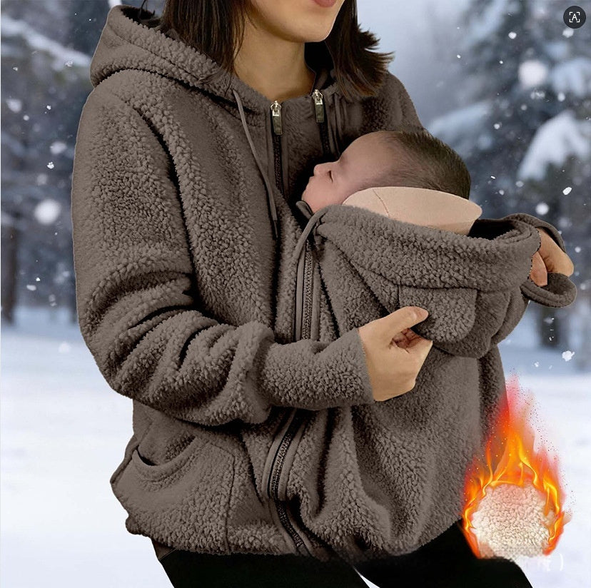 A woman wearing a brown sherpa fleece zip-front hoodie with a baby carrier pocket holding a sleeping baby, set against a snowy outdoor background with a flame-and-ice heat-exchange graphic overlay.