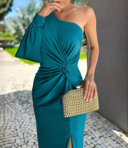 Woman in a teal one-shoulder dress holding a gold clutch outdoors.