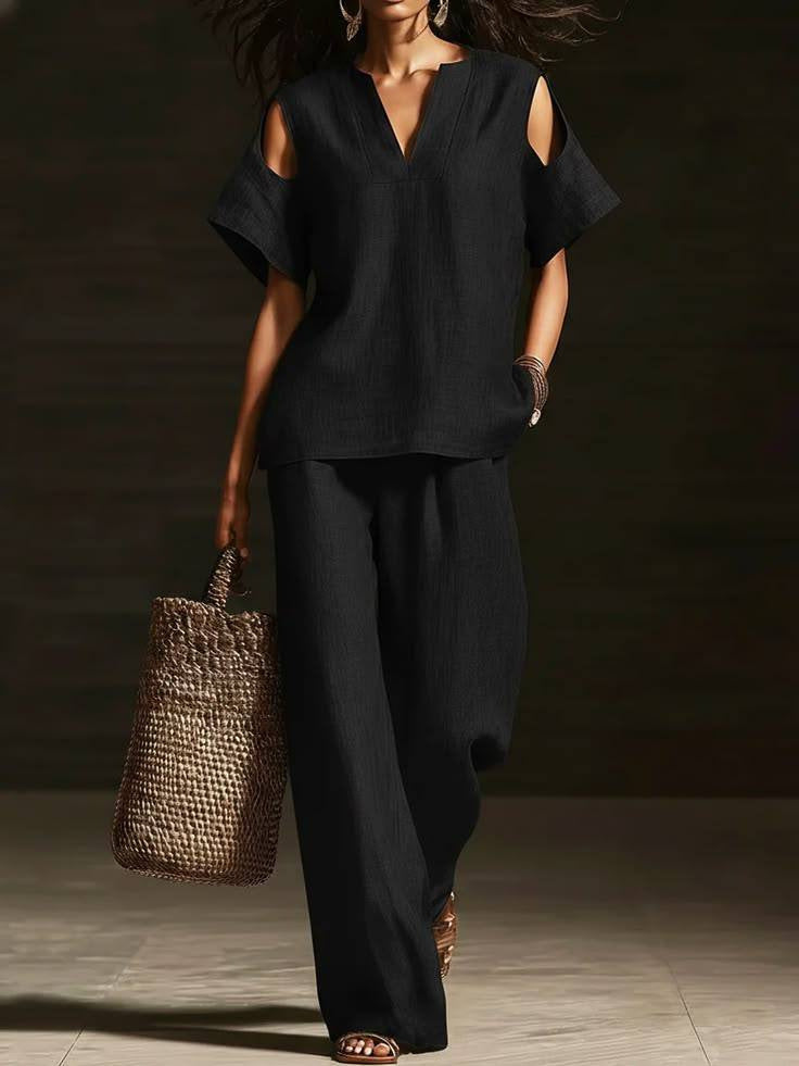 Person wearing a black outfit holding a woven bag against a dark background