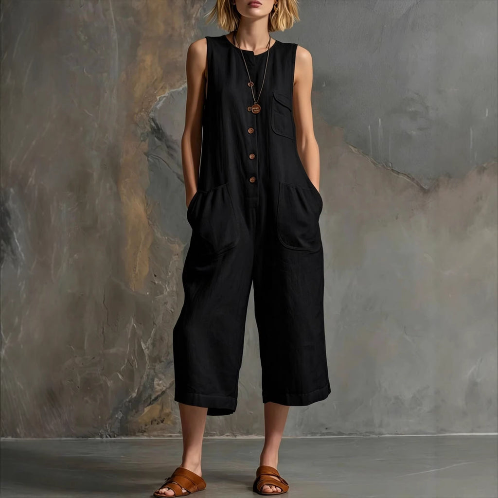Person wearing a black sleeveless jumpsuit against a textured wall.