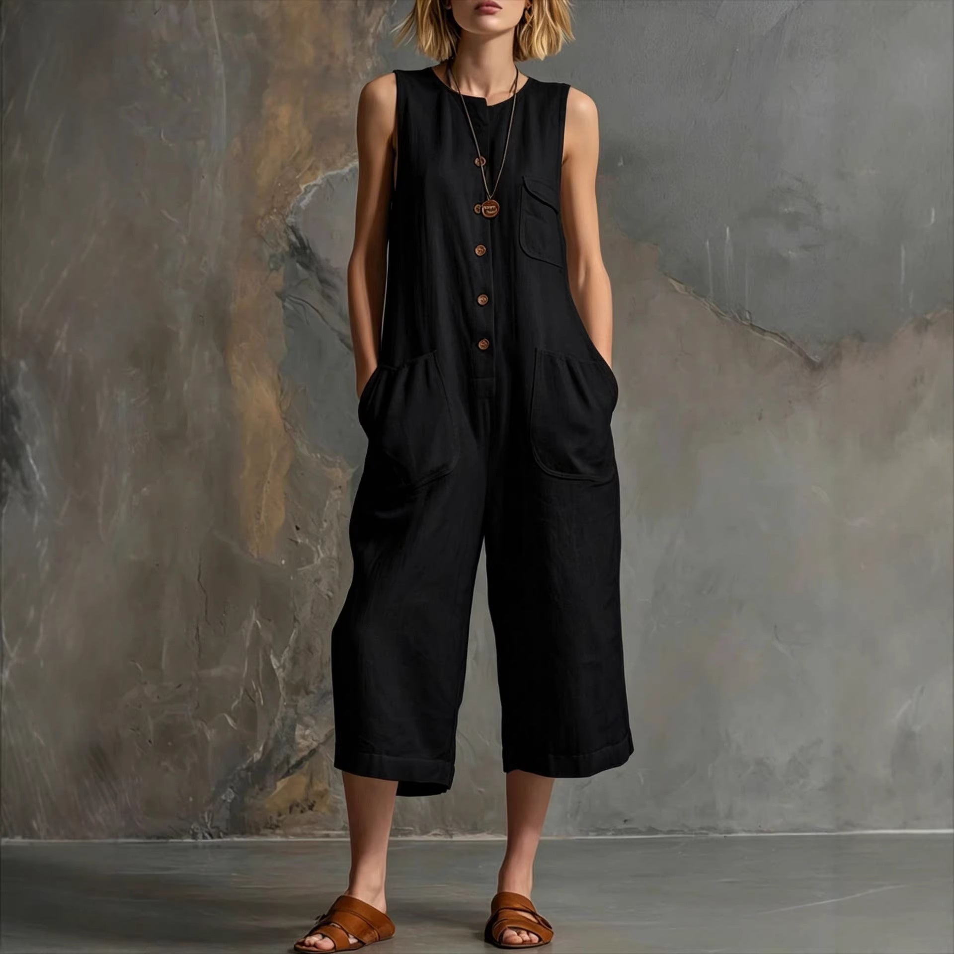 Person wearing a black sleeveless jumpsuit against a textured wall.