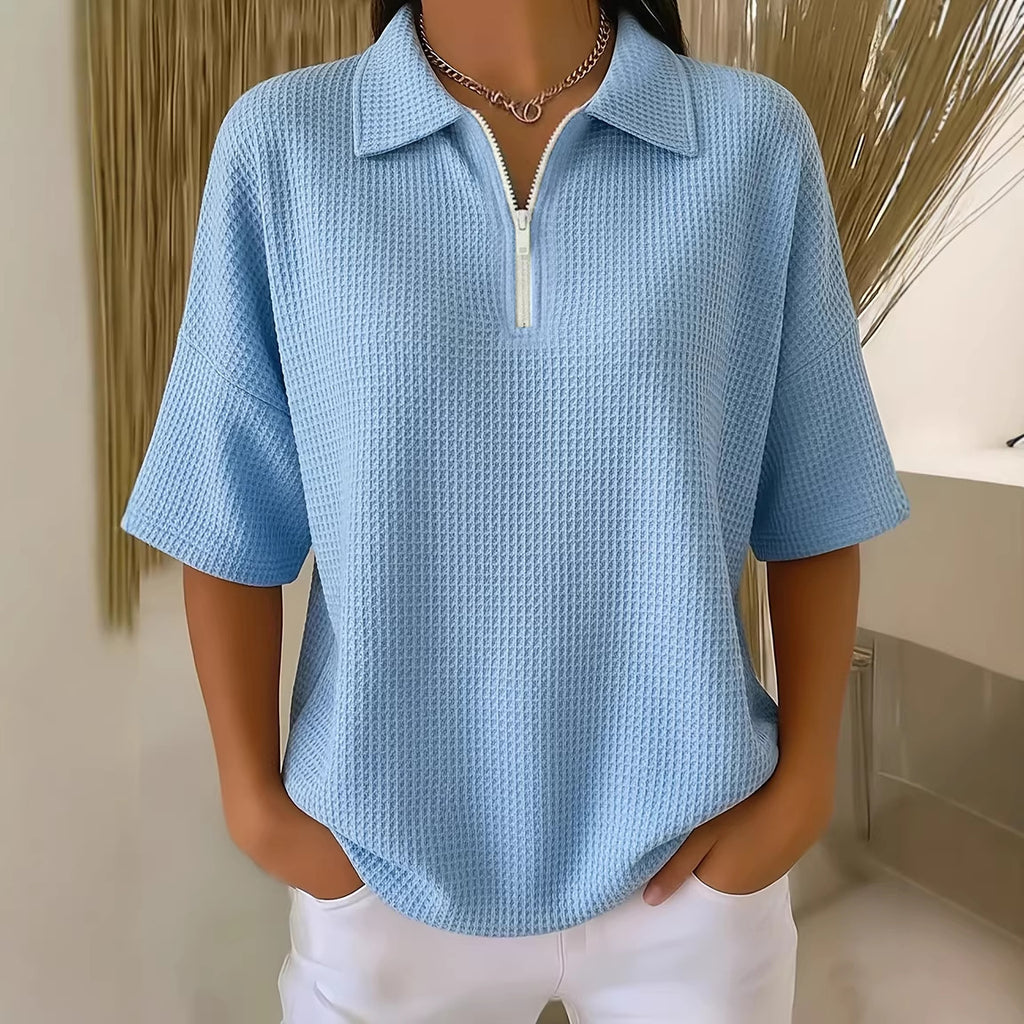 Person wearing a light blue textured shirt with a zipper in a neutral setting