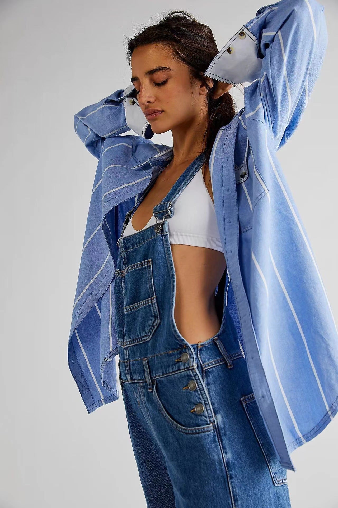 Woman wearing a blue denim jacket and overalls on a plain background
