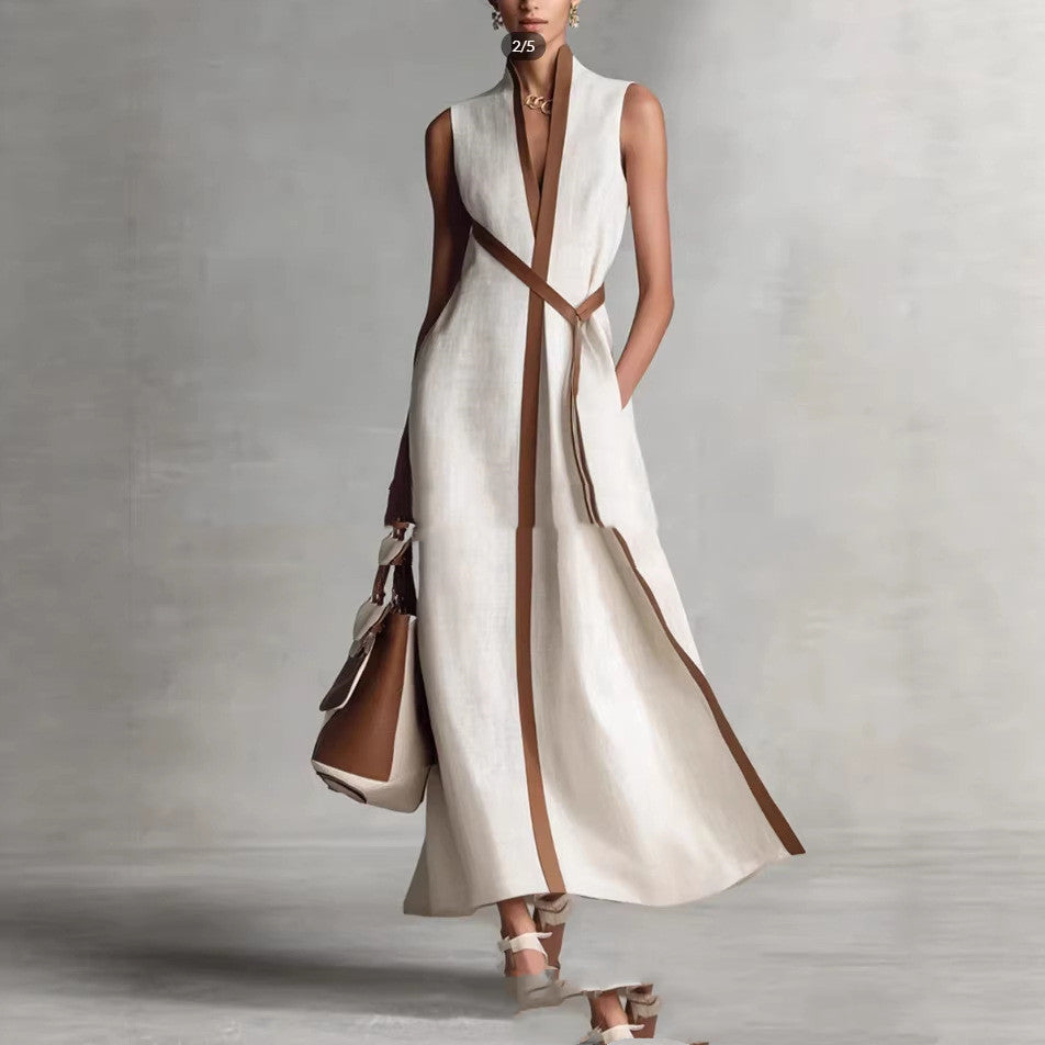 Woman wearing a white dress with brown accents and holding a matching handbag against a gray background