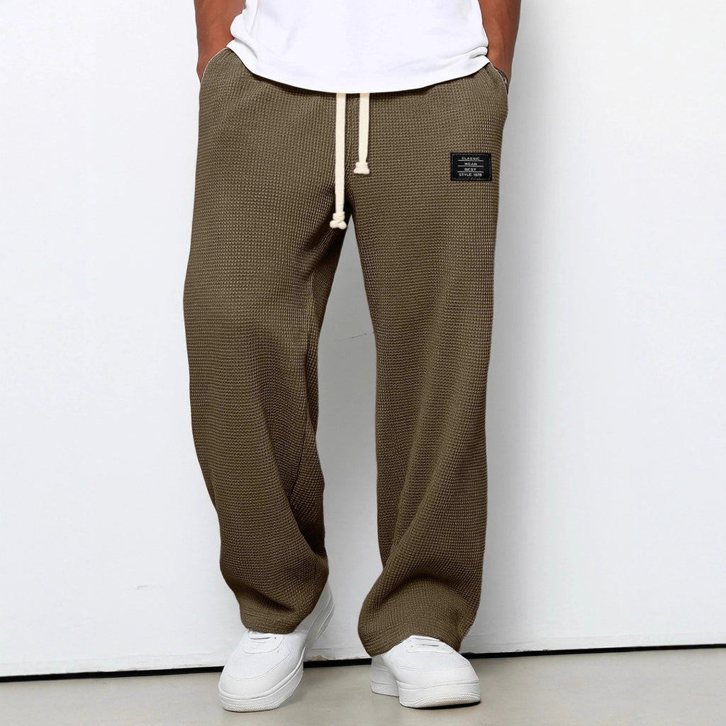 Brown checkered pants with a white label worn by a person on a white background