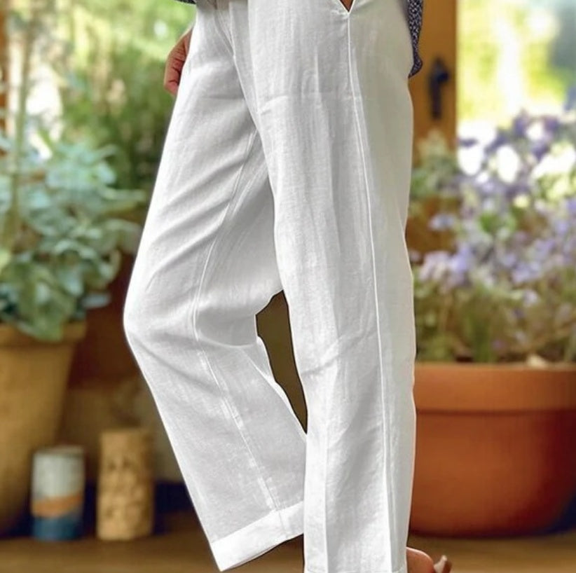 White pants worn by a person with a blurred background of plants and pots.