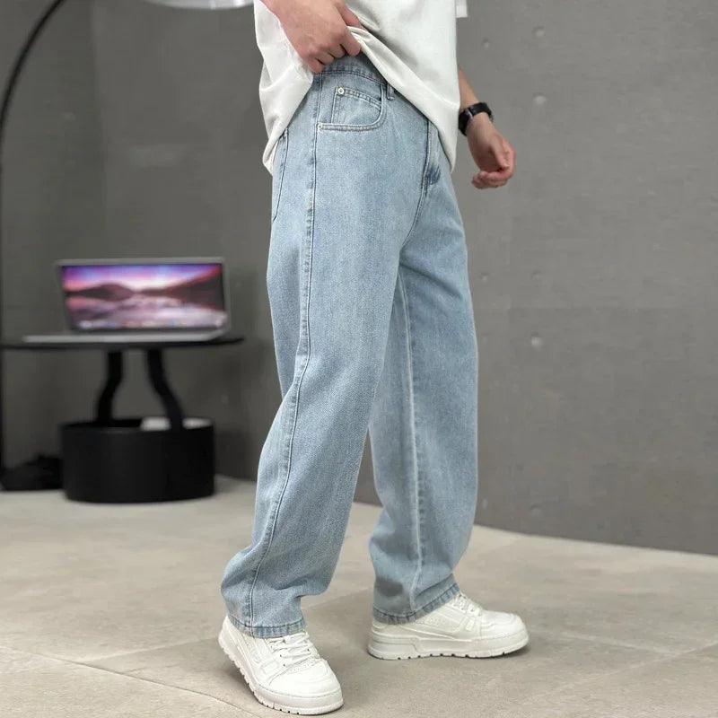 Person wearing light blue jeans and white sneakers in a minimal indoor setting.