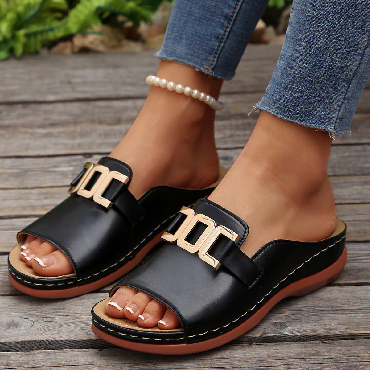 Black sandals with gold buckles worn on a wooden floor