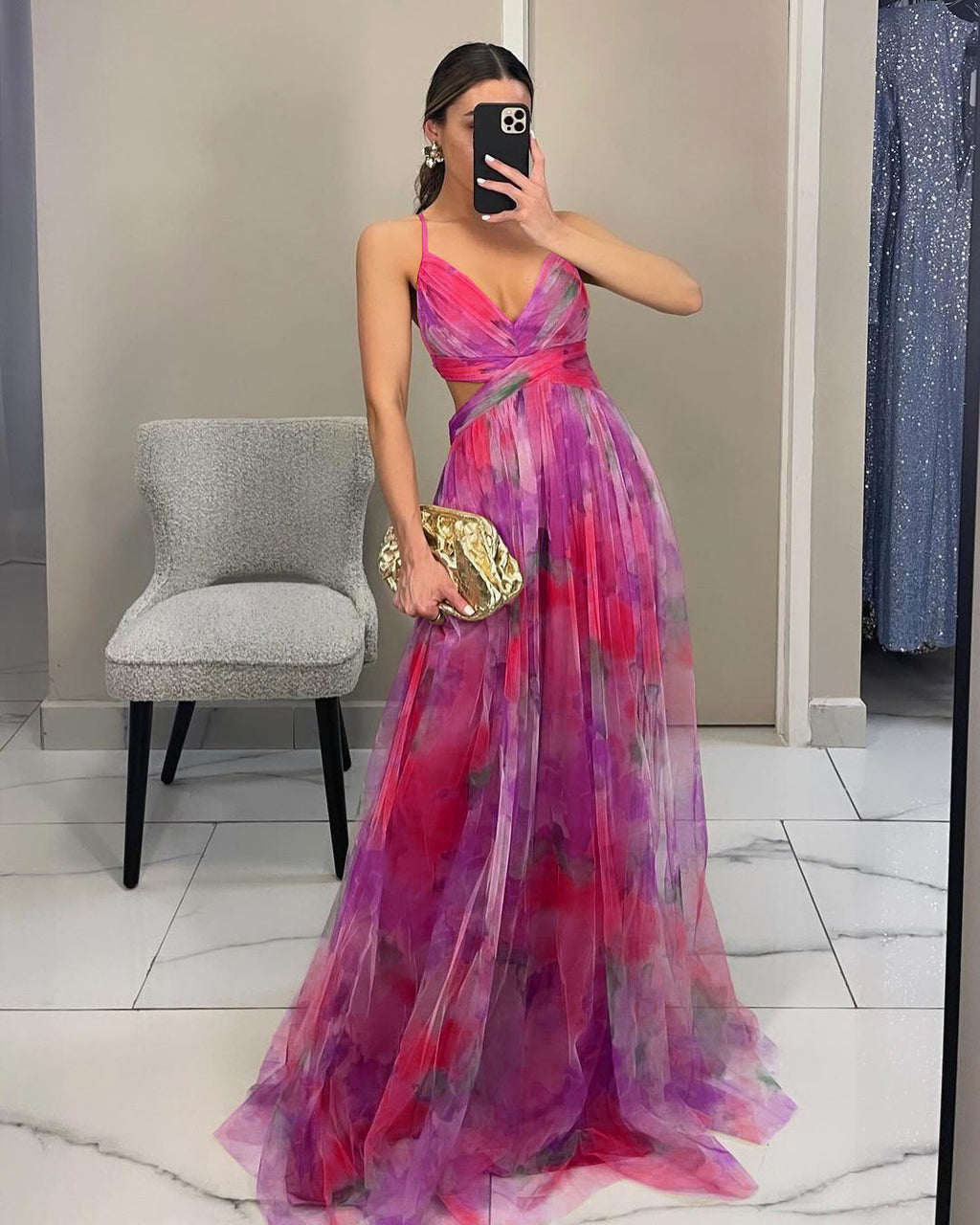 Woman wearing a colorful dress with a gold clutch in a room.