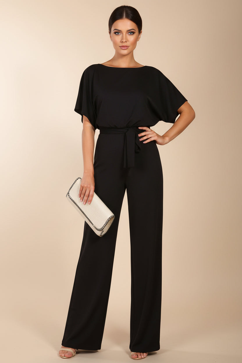 Woman wearing a black jumpsuit holding a clutch against a white background