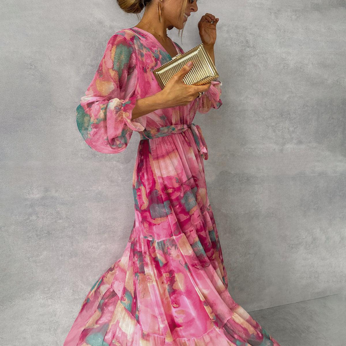 Woman wearing a pink floral dress holding a gold clutch against a gray background