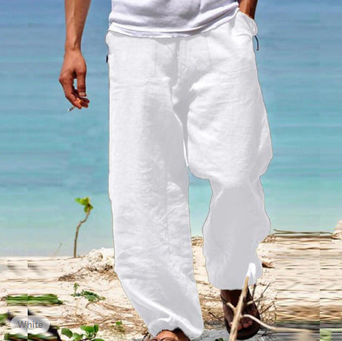 Person wearing white pants standing on a beach with clear blue water in the background