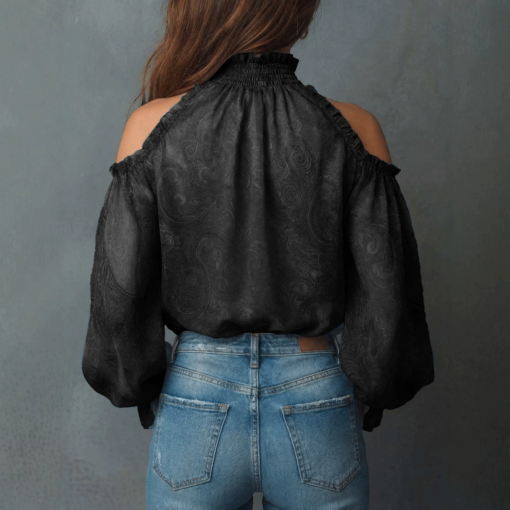 Person wearing a black blouse with sheer sleeves and blue jeans against a gray background