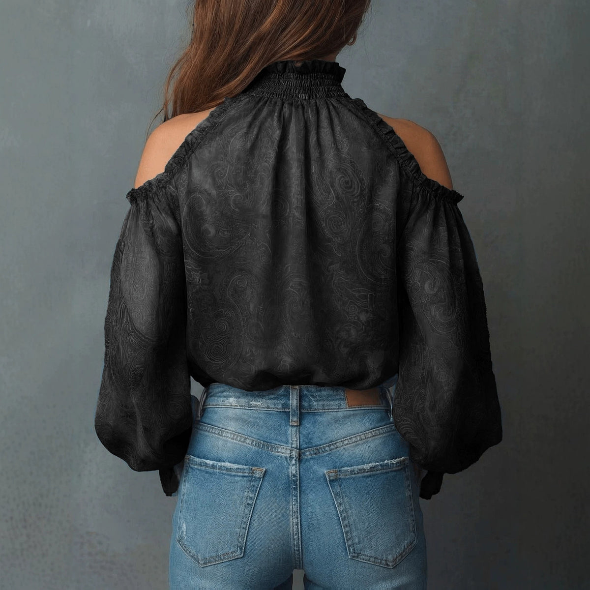 Person wearing a black blouse with sheer sleeves and blue jeans against a gray background