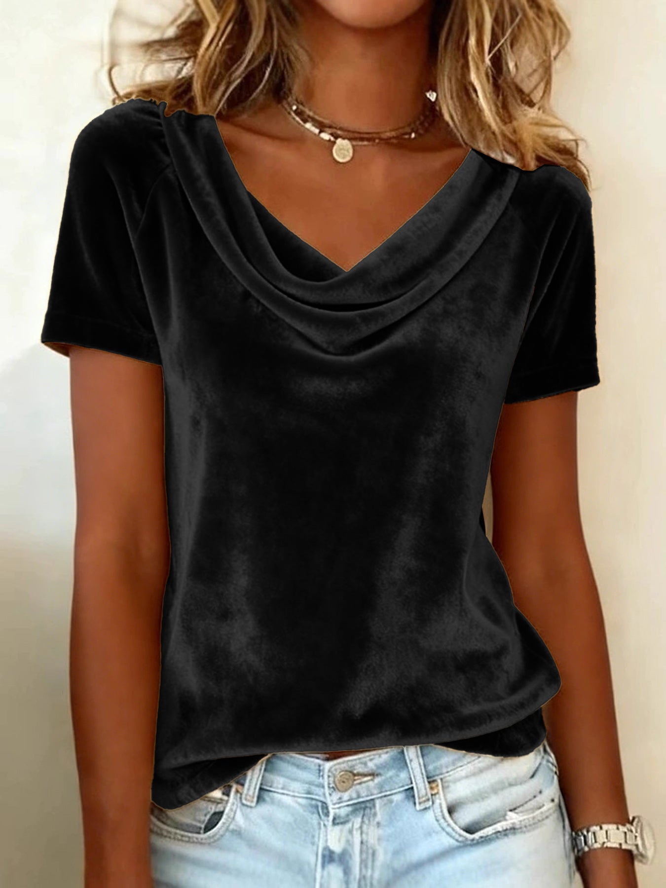Person wearing a black cowl-neck t-shirt and light blue jeans against a neutral background