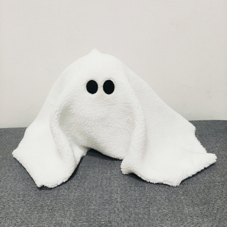 White ghost-shaped pillow with black eyes on a gray surface
