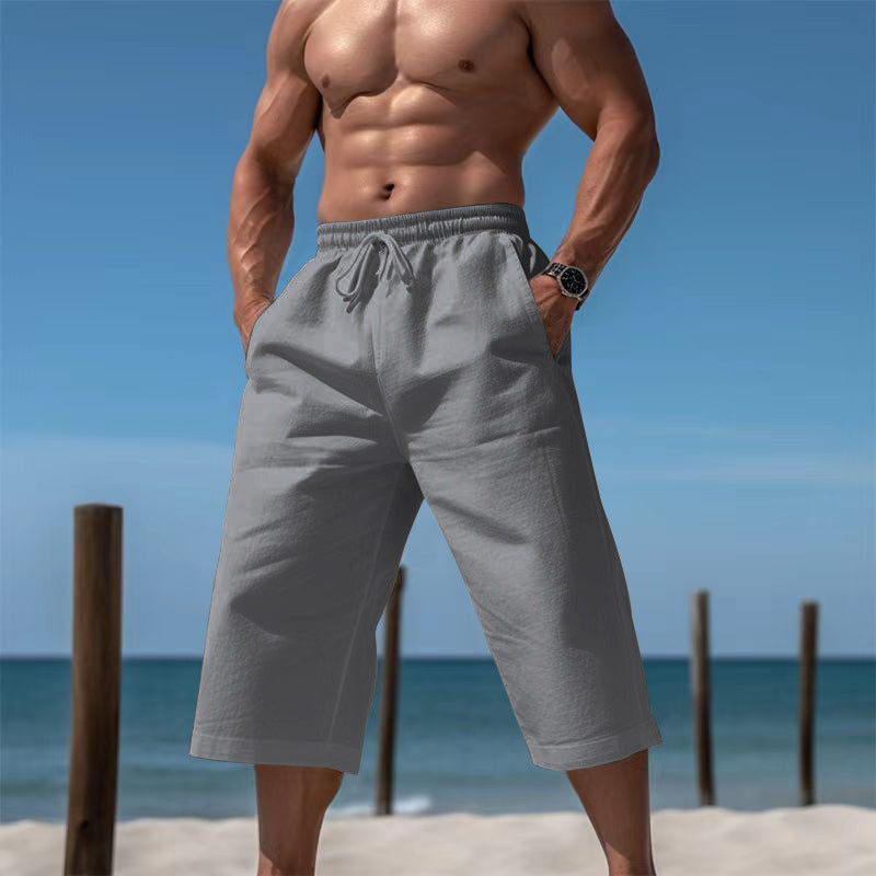 Man wearing gray shorts on a beach with clear blue sky and ocean.