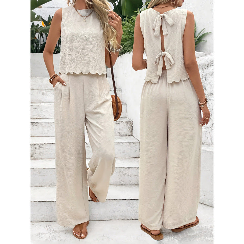 Two women wearing beige sleeveless tops and wide-leg pants on a white staircase.