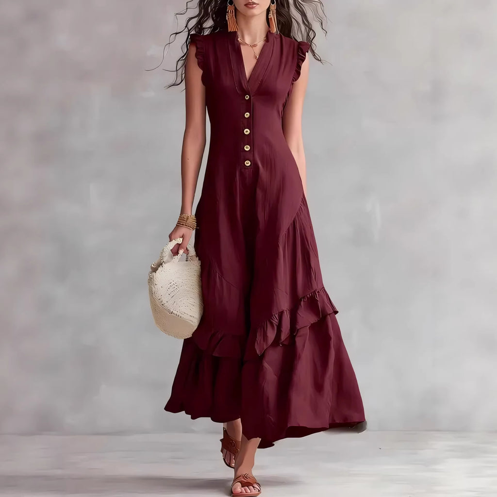 Woman wearing a burgundy dress with ruffled layers, holding a beige handbag against a plain background.