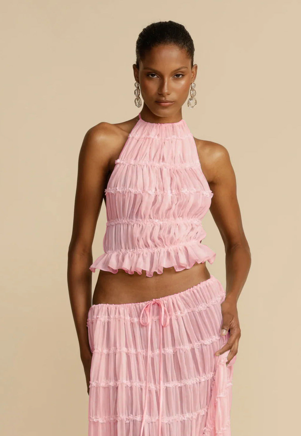 Woman wearing a pink ruffled top and skirt set against a beige background