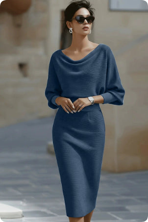Woman wearing a blue outfit with sunglasses against a stone wall background