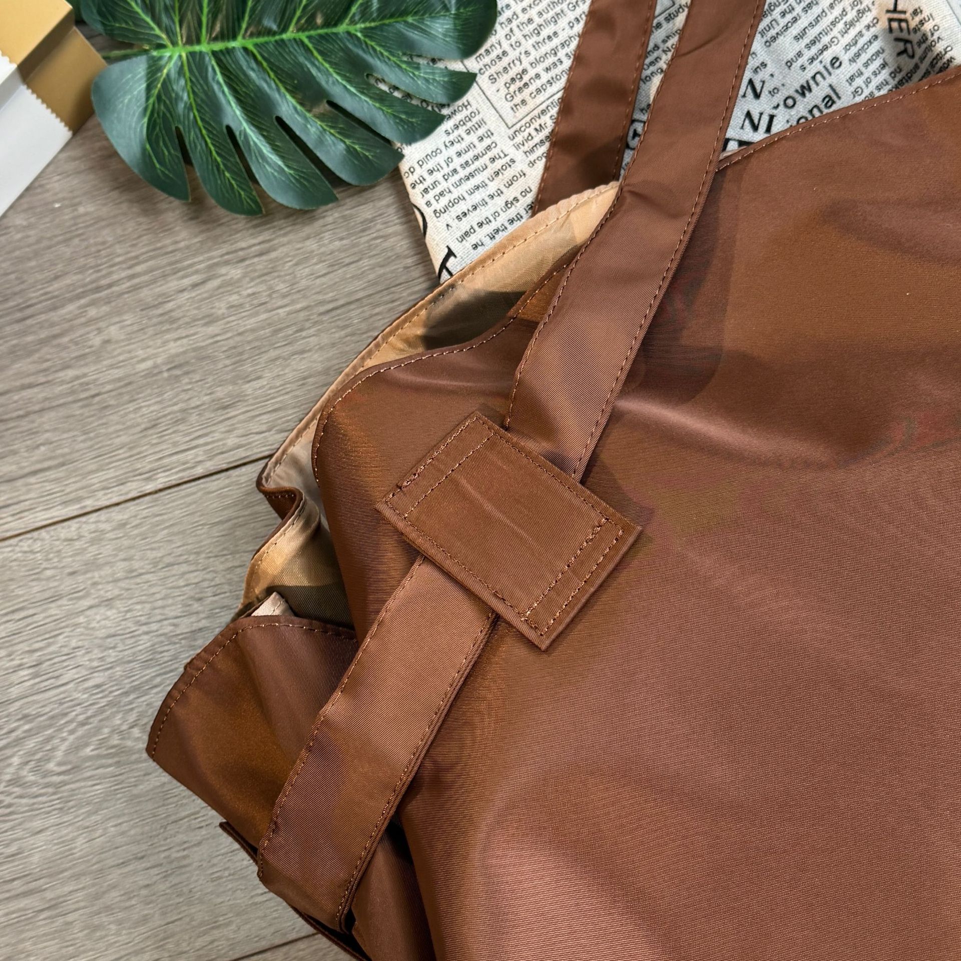 Brown leather bag on a wooden surface with a plant and newspaper in the background
