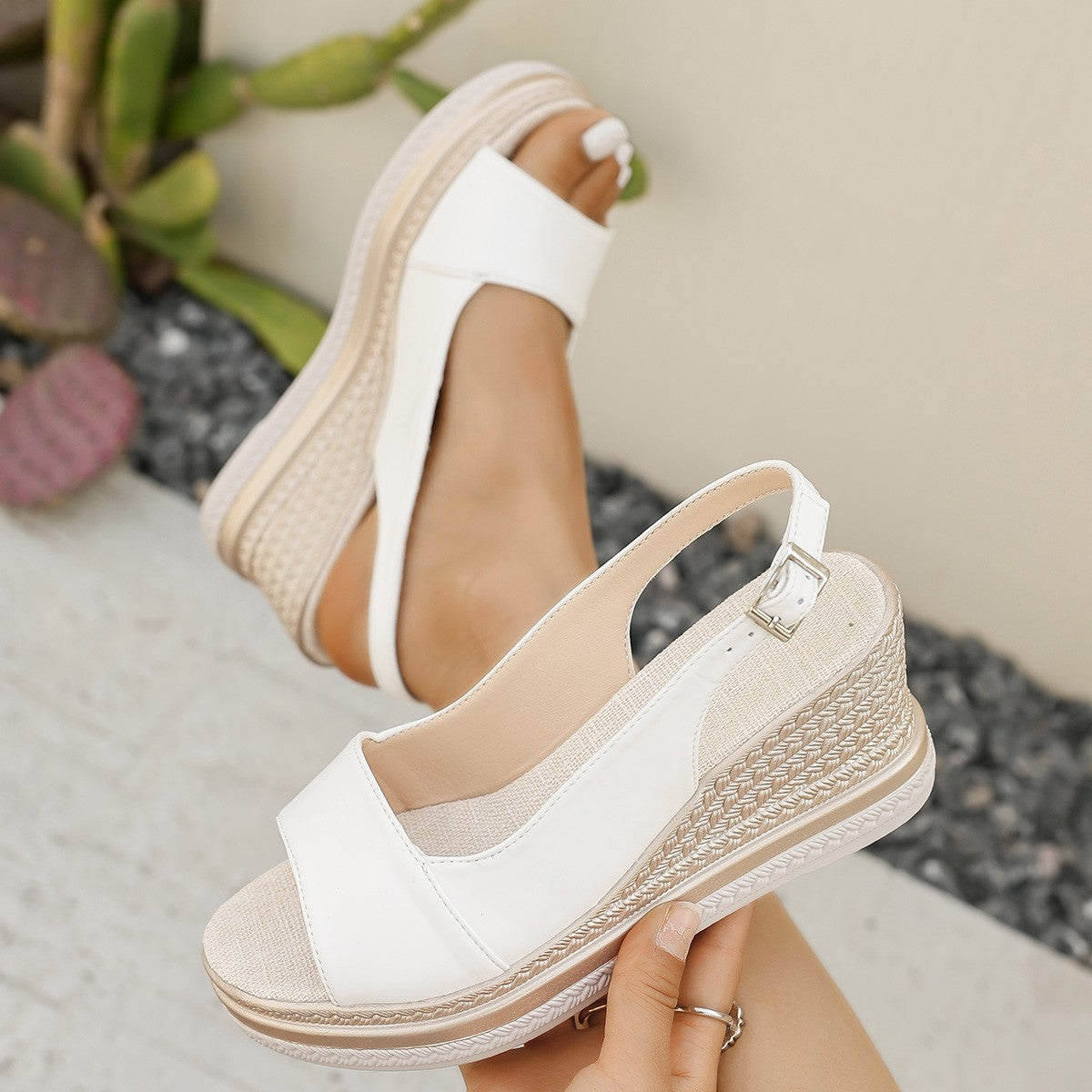 White wedge sandals with espadrille details worn by a person, with a blurred background.
