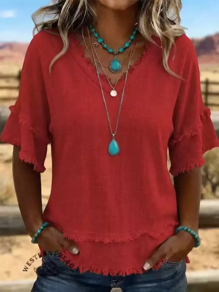 Person wearing a red blouse with ruffled sleeves and turquoise jewelry outdoors.