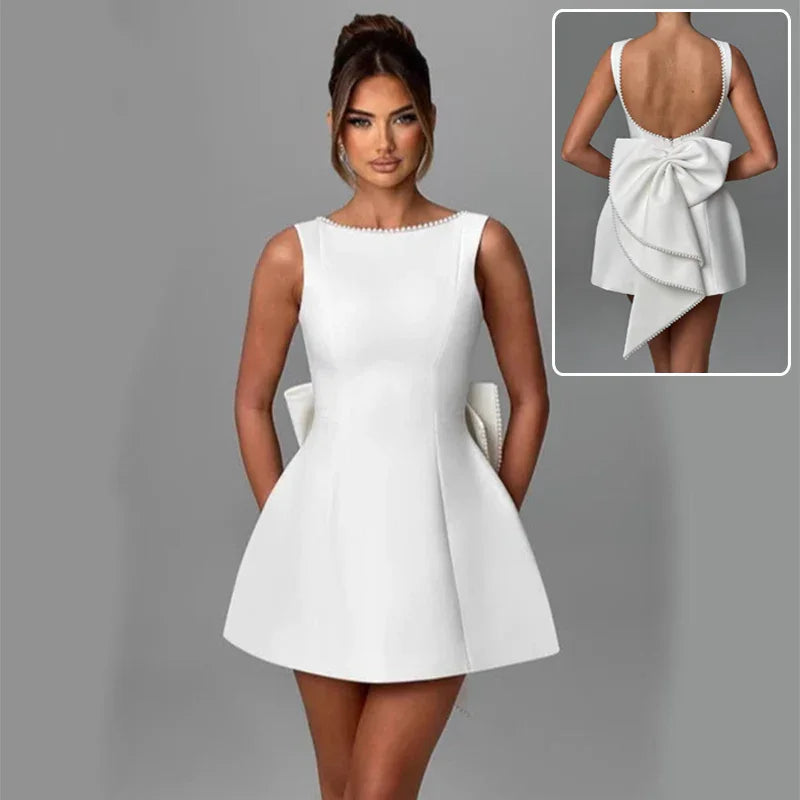 White dress with a large bow detail on the back, worn by a model against a gray background.
