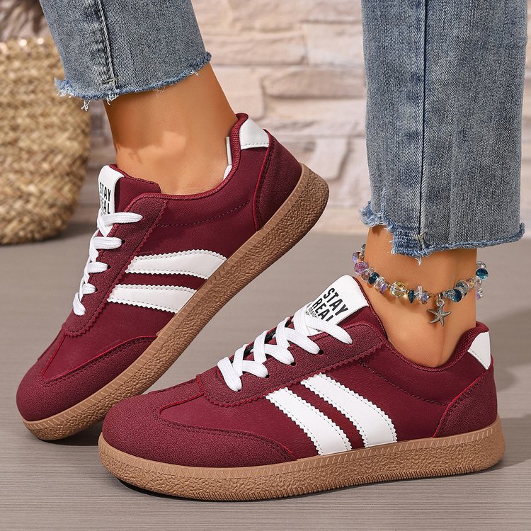Maroon sneakers with white stripes worn by a person on a neutral background