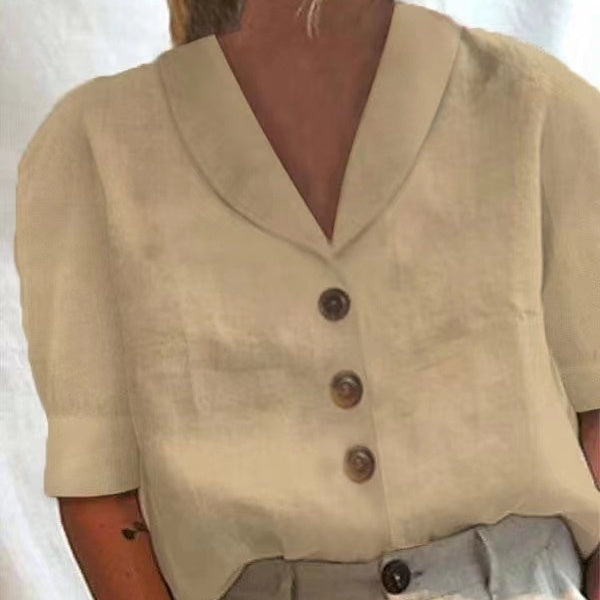 A close-up of a person wearing a short-sleeve cream-colored linen top with a V-neck and three dark brown buttons down the front.