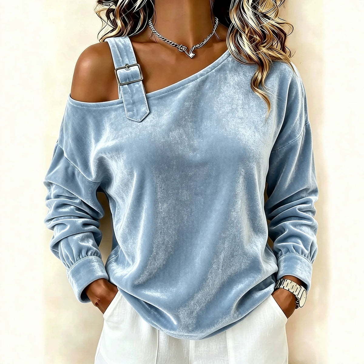 A woman wearing a light blue off-the-shoulder velvet long-sleeve top with a decorative strap detail on one shoulder, paired with white pants.